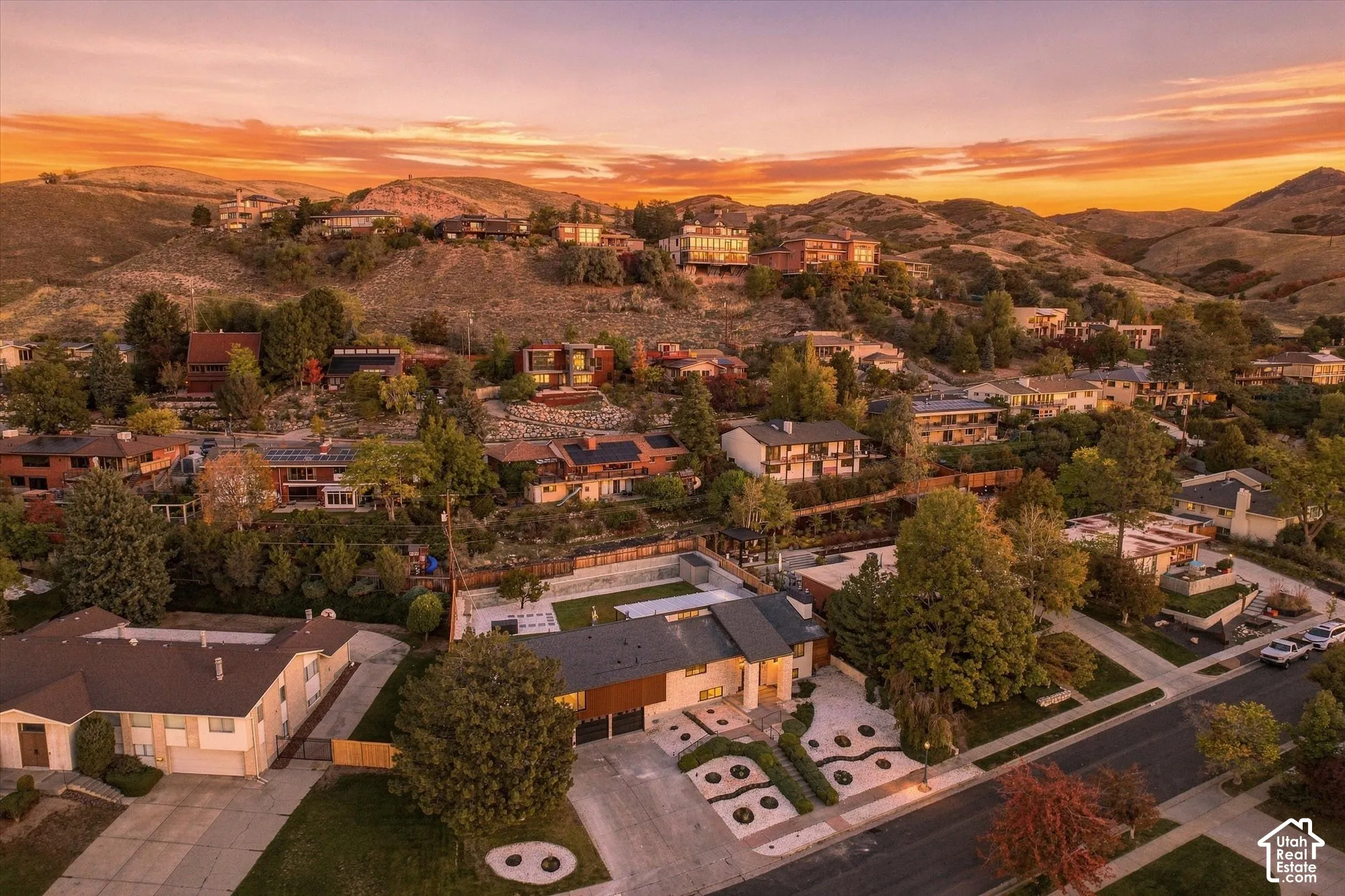 Aerial perspective showcasing a hillside residential setting with mountain topography, mature landscaping, multi-level exterior architecture, and an integrated paved driveway