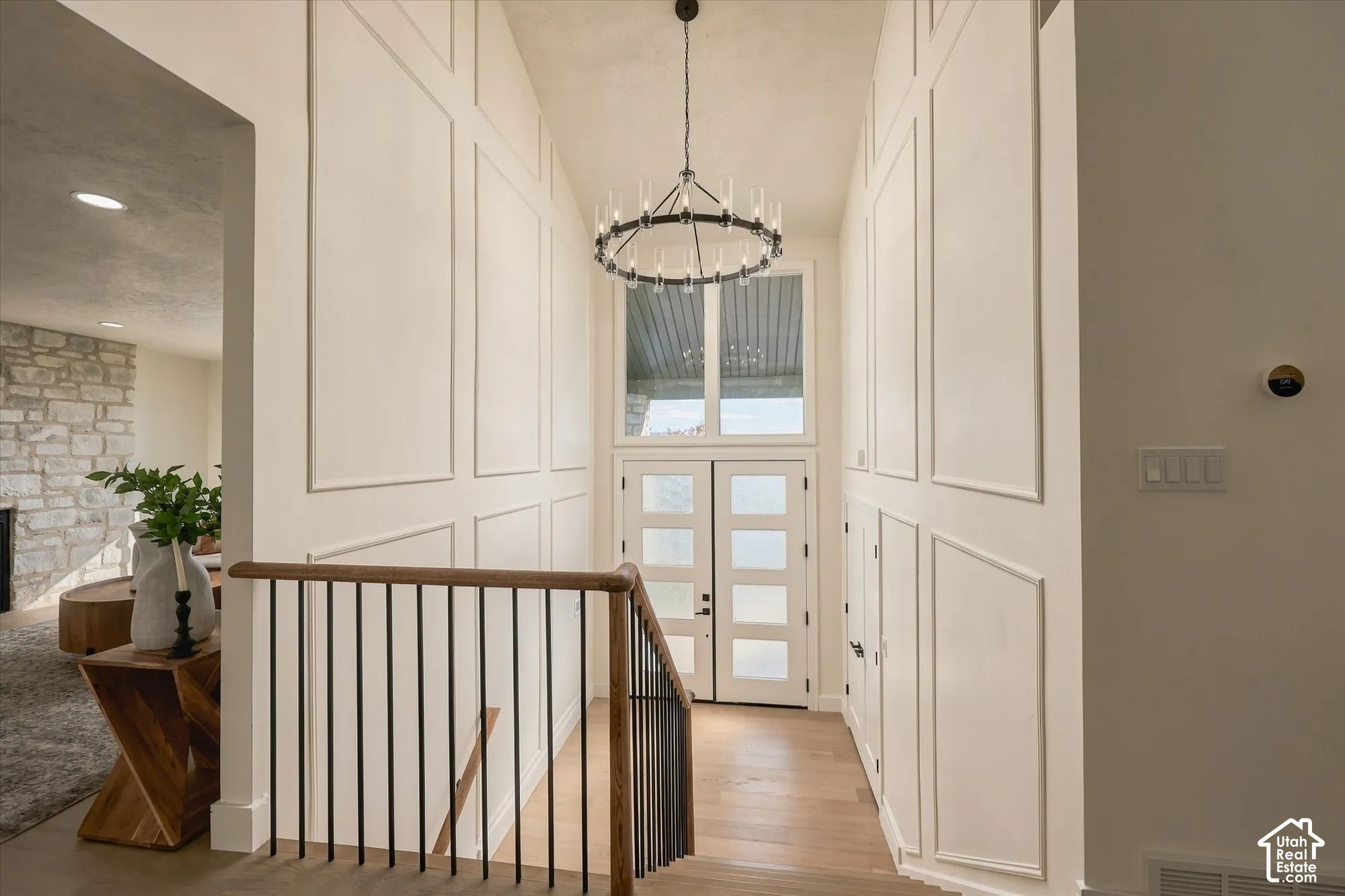 Foyer featuring board-and-batten wall detailing, high vaulted ceilings, double entry doors with glass panels, a circular tiered chandelier, and wood-finish flooring