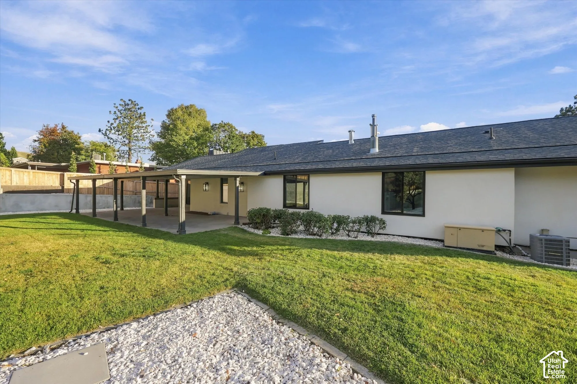 Rear exterior featuring a covered patio, smooth-finish siding, asphalt shingle roof, expansive lawn, and stone landscaping accents
