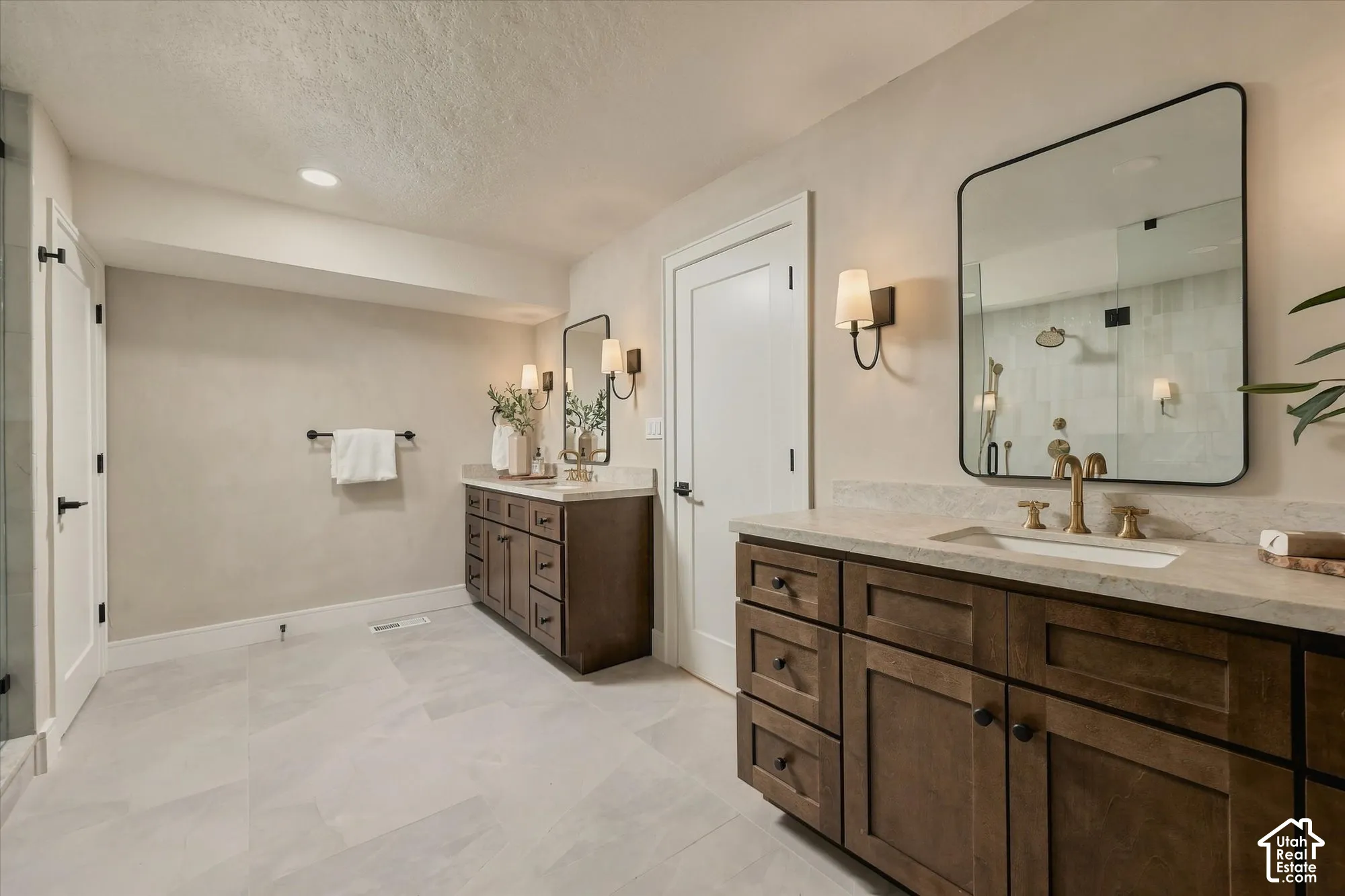 Dual vanities featuring dark-stained cabinetry, stone-style countertops, rectangular undermount sinks, brass-toned fixtures, and rectangular mirrors with black frames