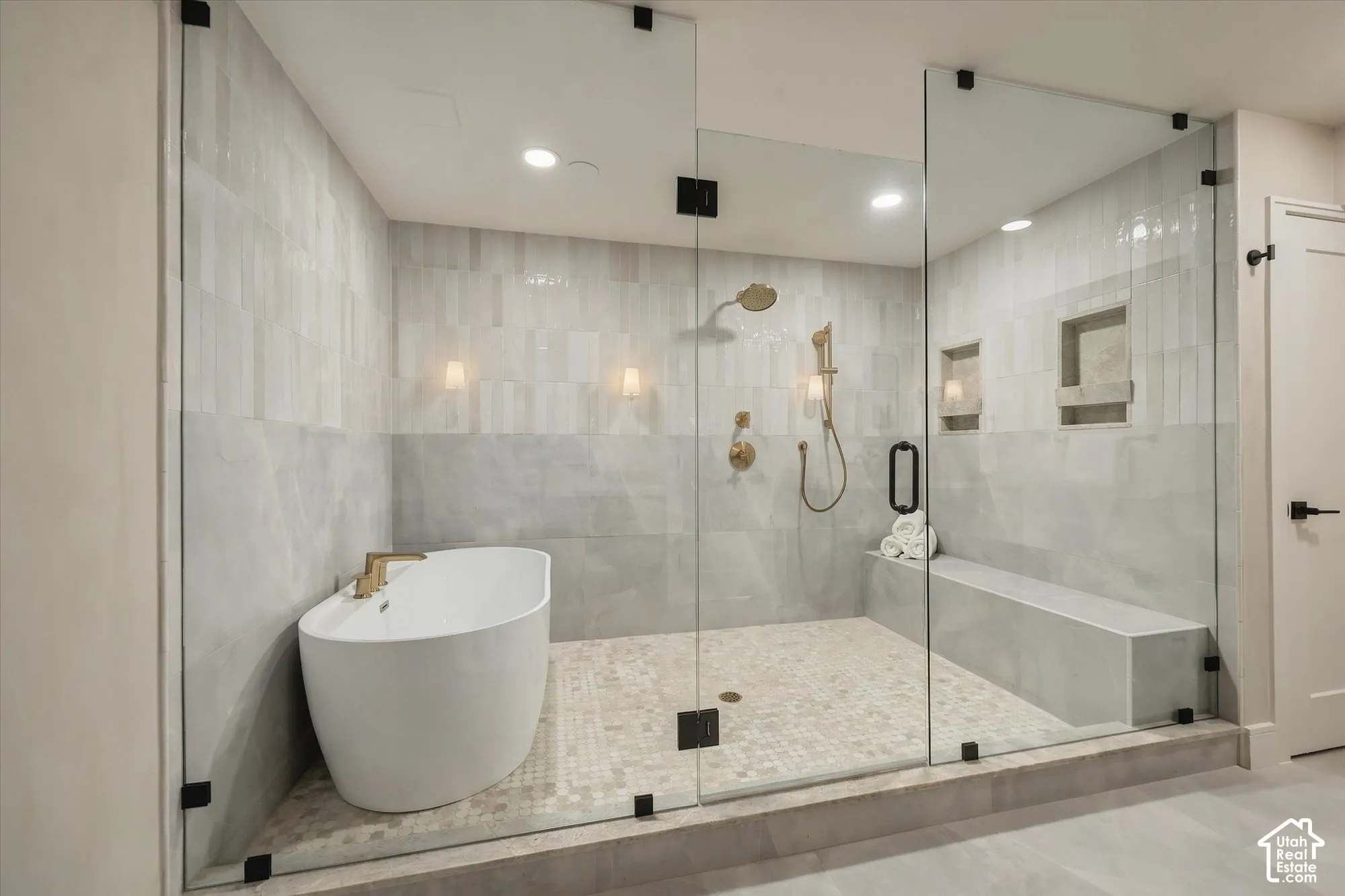 Glass-enclosed wet room featuring a freestanding soaking tub, rainfall showerhead, handheld shower fixture, built-in tiled bench, and dual recessed wall niches