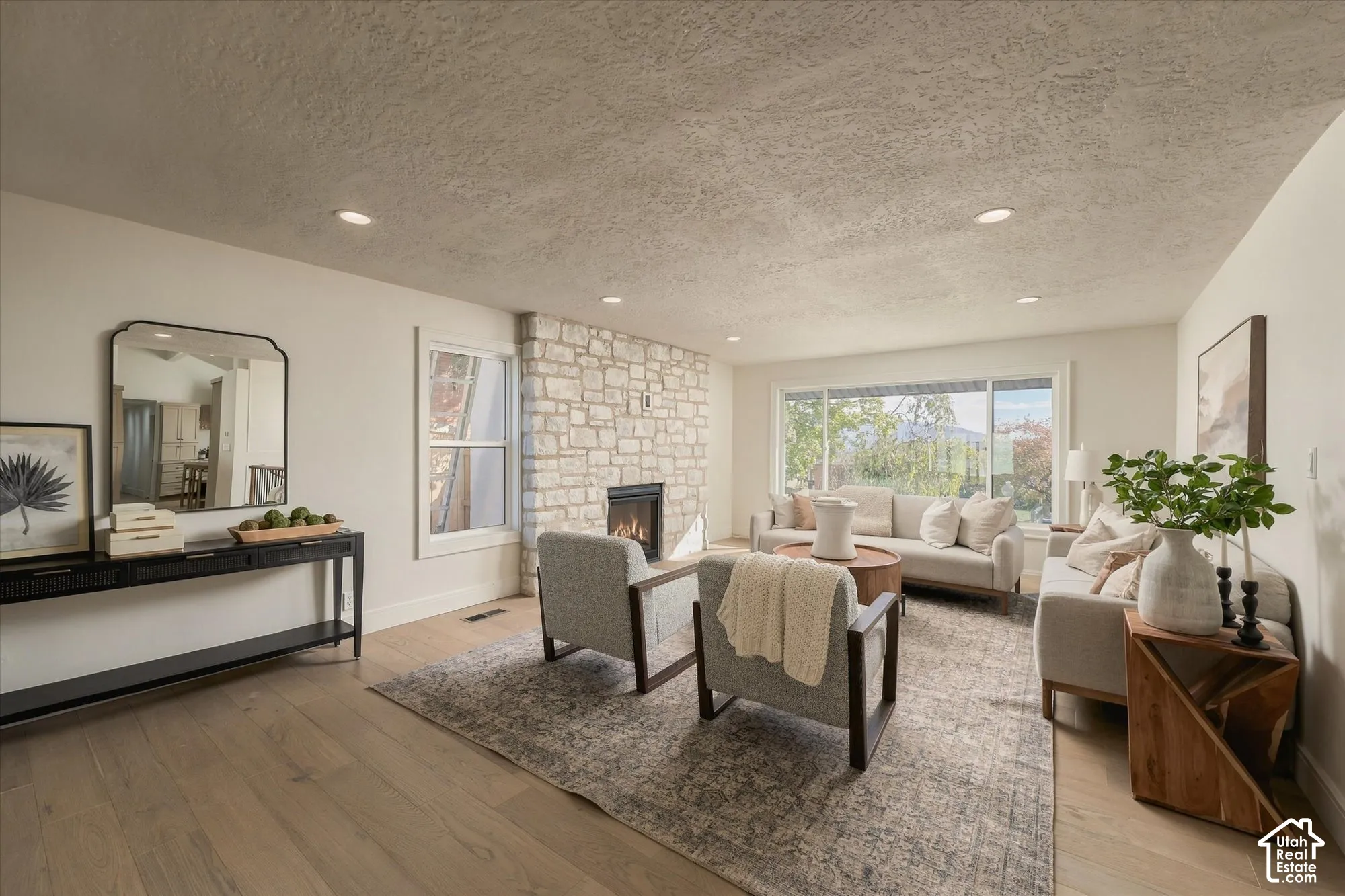 Living room featuring wood-finish flooring, a full-height stone fireplace surround, recessed lighting, and large windows