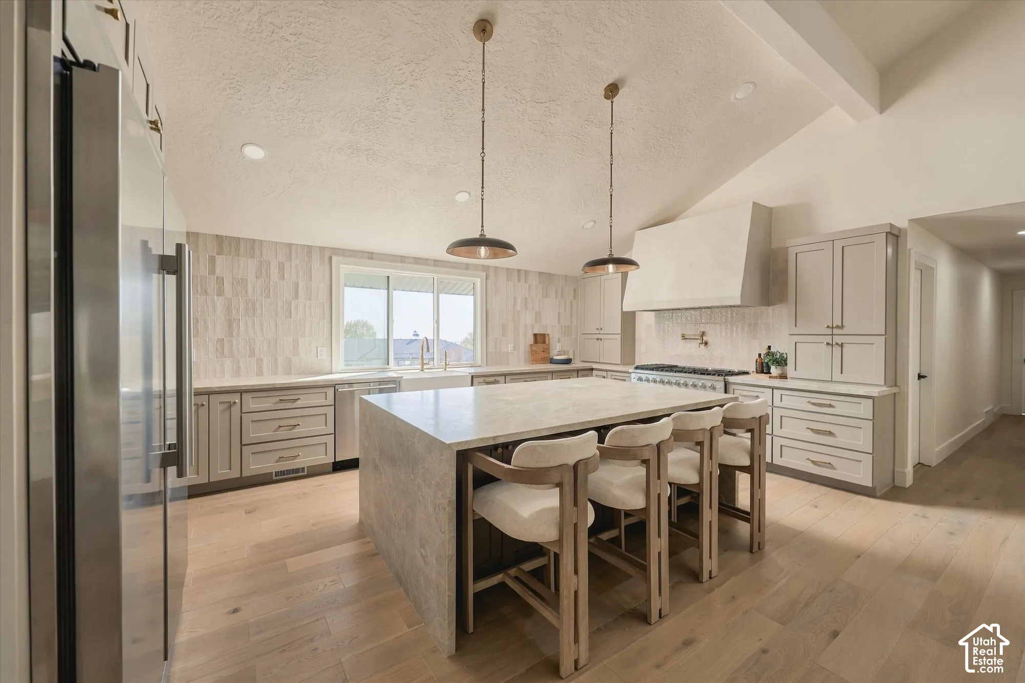 Kitchen featuring a large central island with a stone-finish countertop, custom-height cabinetry, a built-in range hood, a farmhouse-style sink, and wood-finish flooring