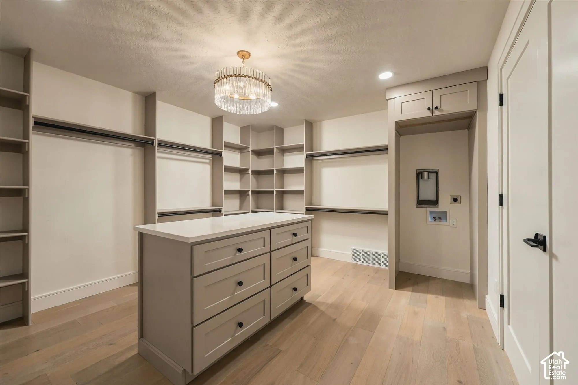 Custom walk-in closet featuring extensive built-in shelving, a center island with quartz countertop and storage drawers, wood-finish flooring, and a decorative crystal-style chandelier