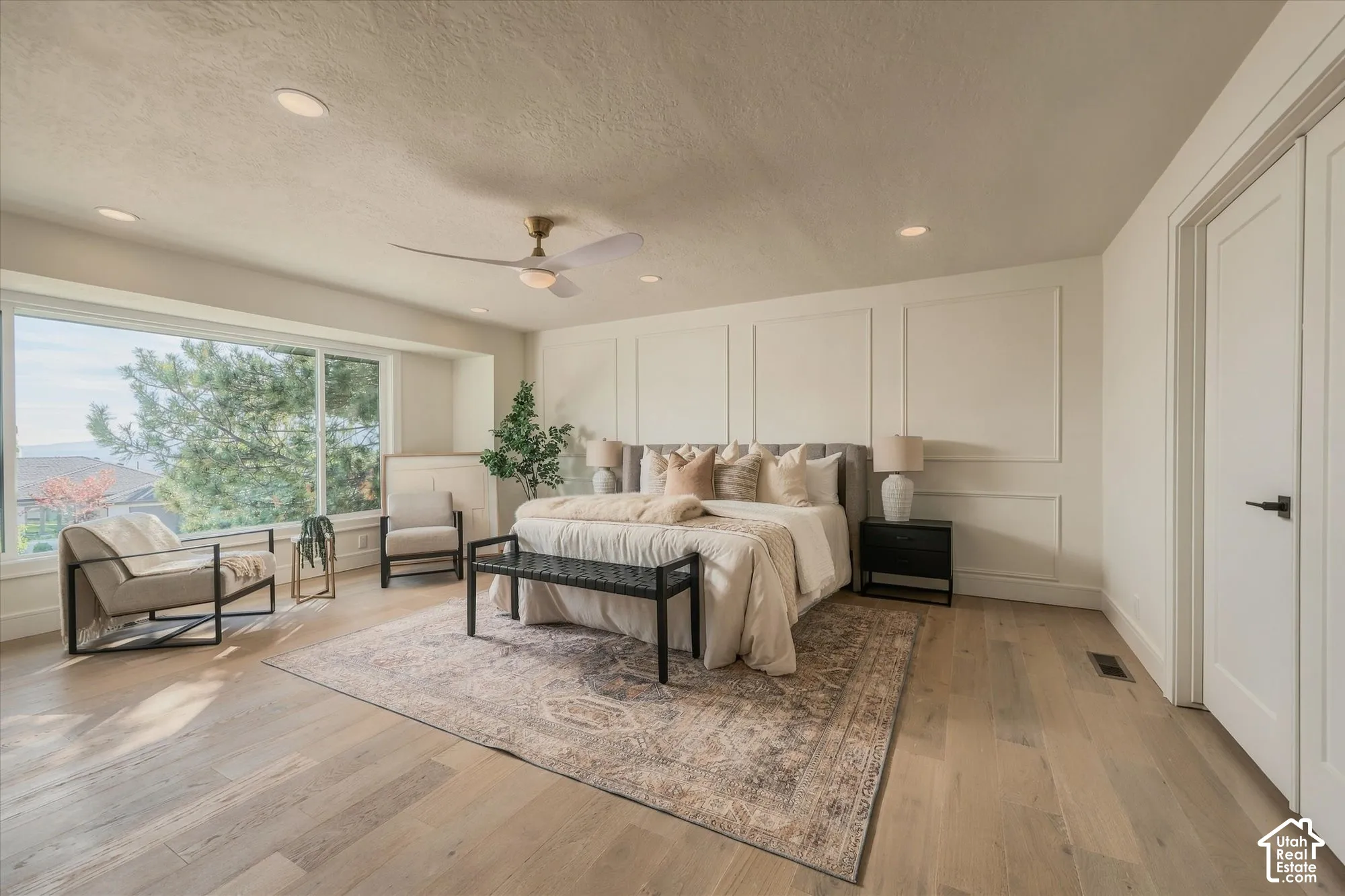 Light-filled room featuring wood-finish flooring, wainscot wall molding, a multi-blade ceiling fan, and a large picture window