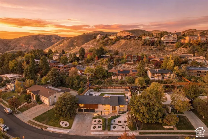 Aerial perspective of a multi-level residence featuring wood and stone exterior cladding, an attached garage, a tiered front landscape with retaining walls, and a large elevated rear deck