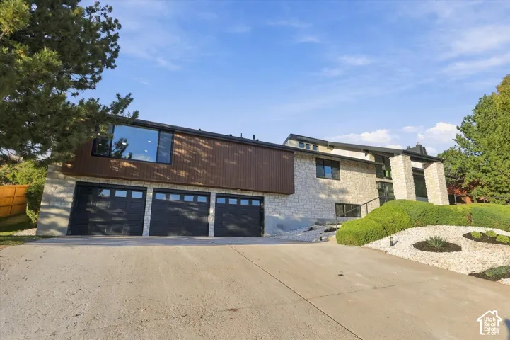 Multi-level exterior featuring stone masonry, vertical wood-finish siding, a three-car garage with glass-panel doors, and xeriscaped landscaping