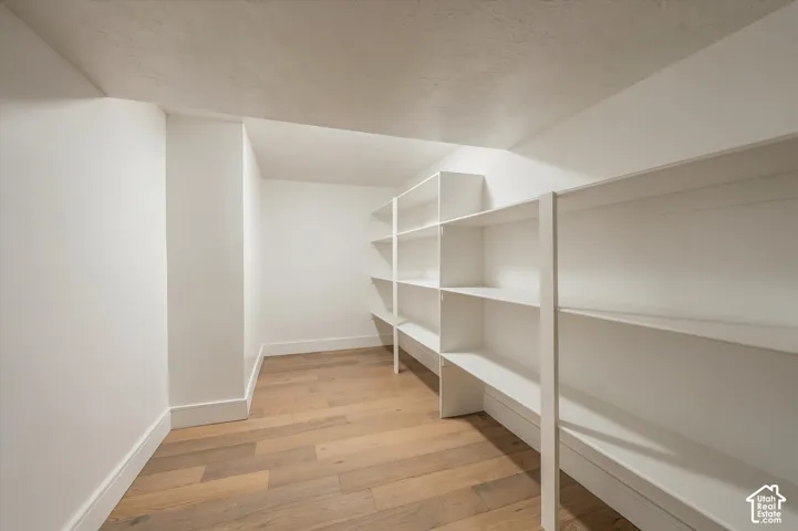 Storage area featuring white built-in shelving and wood-finish flooring
