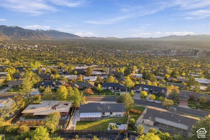 Aerial perspective featuring an expansive lawn, concrete patio, semi-covered pergola, mature trees, and an expansive mountain range backdrop