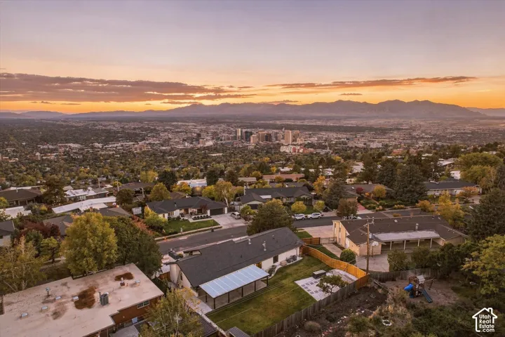 Aerial perspective featuring a shingled roof, an expansive rear patio with a covered pergola structure, a paved hardscape area, and a prominent mountain range backdrop