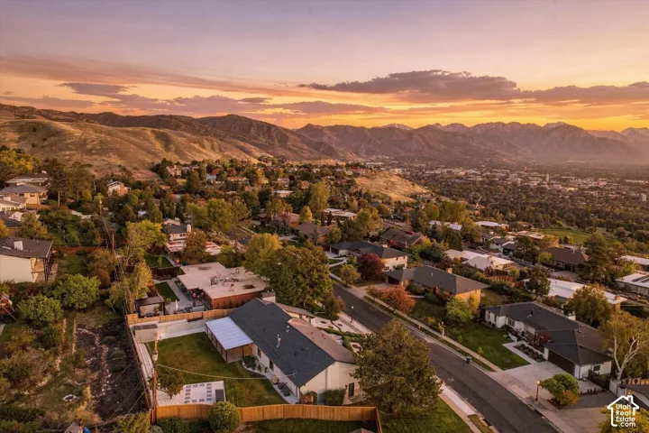 Aerial perspective featuring a multi-level residential property with a fenced backyard, hardscaped patio, and expansive mountain range backdrop