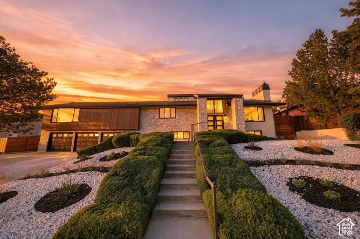 Multi-level exterior featuring a stone-clad facade, horizontal wood paneling, an integrated garage, and a tiered rock garden with mature landscaping