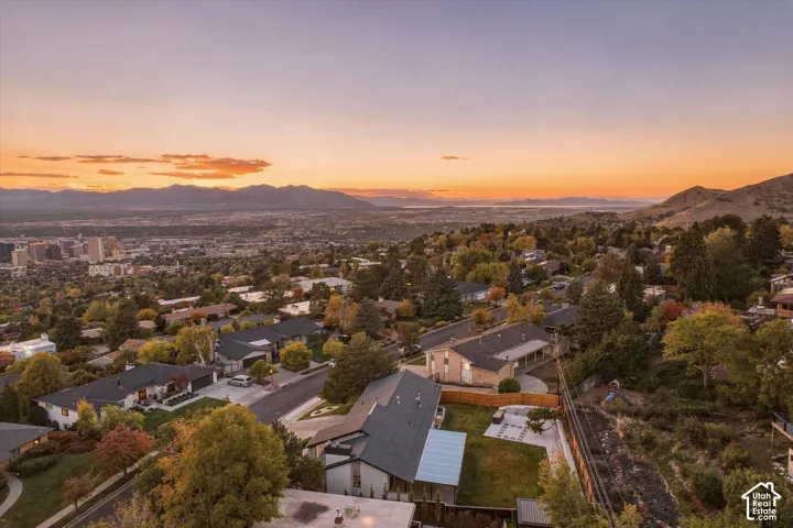Elevated hillside property featuring a paved rear patio, mature trees, multi-level rooflines, and a mountain and valley backdrop