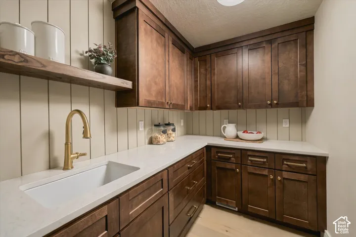 Custom-stained cabinetry with brass-tone hardware, stone-finish countertops, vertical panel wall treatment, built-in floating shelf, and undermount farmhouse sink with a high-arch brass-tone faucet