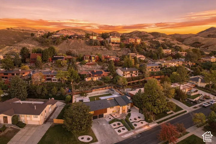 Aerial perspective showcasing a hillside residential setting with mountain topography, mature landscaping, multi-level exterior architecture, and an integrated paved driveway