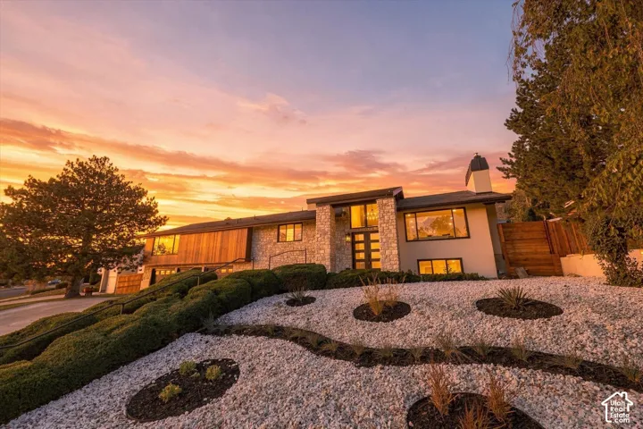 Exterior elevation featuring stone masonry facade, horizontal wood paneling, multi-pane transom windows, and landscaped rock garden with manicured shrubbery