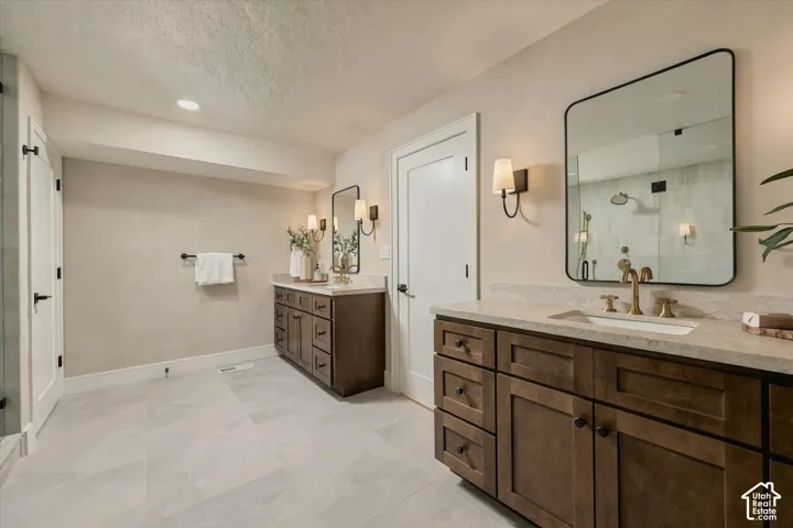 Dual vanities featuring dark-stained cabinetry, stone-style countertops, rectangular undermount sinks, brass-toned fixtures, and rectangular mirrors with black frames