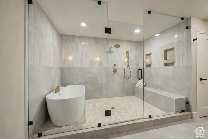 Glass-enclosed wet room featuring a freestanding soaking tub, rainfall showerhead, handheld shower fixture, built-in tiled bench, and dual recessed wall niches
