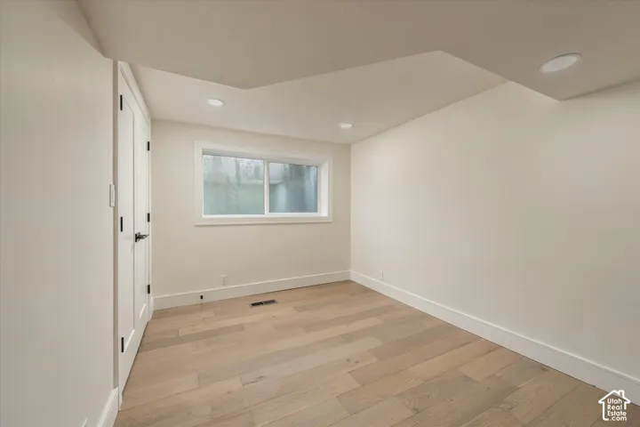Neutral-toned room featuring wood-finish flooring, recessed lighting, and a dual-panel door with matte black hardware