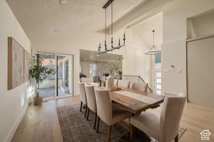 Dining area featuring vaulted ceilings, wood-finish flooring, paneled accent wall, matte black linear chandelier, and sliding glass door