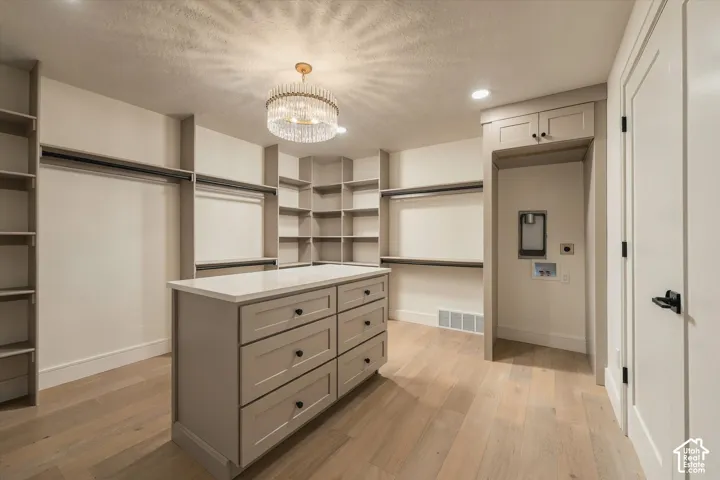 Custom walk-in closet featuring extensive built-in shelving, a center island with quartz countertop and storage drawers, wood-finish flooring, and a decorative crystal-style chandelier