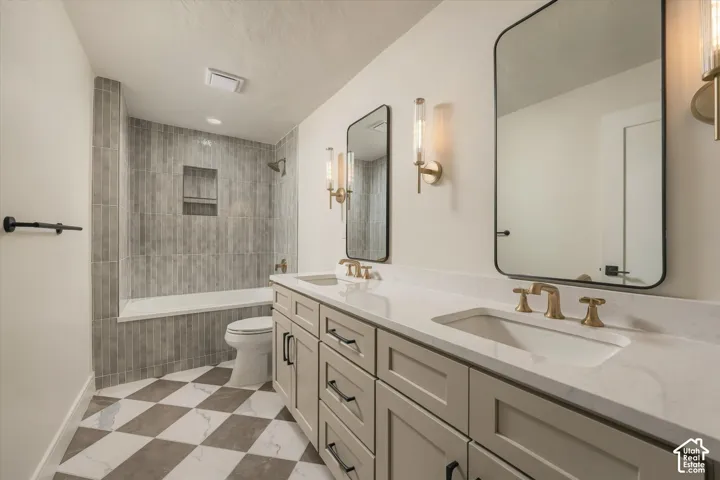 Double vanity with quartz countertops, integrated sinks, brass fixtures, and framed mirrors, paired with a shower-tub combination featuring floor-to-ceiling tilework and a built-in recessed niche