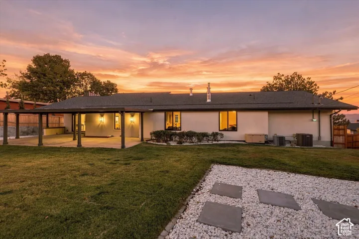 Exterior featuring a covered patio, paved walkway, manicured lawn, and low-maintenance stone landscaping