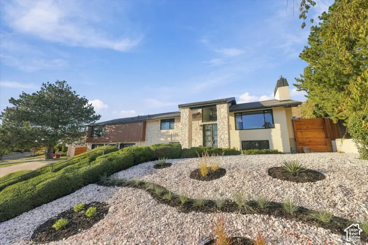 Mid-century modern exterior featuring natural stone veneer, textured wood paneling, a concrete chimney, and tiered low-maintenance landscaping with decorative stone mulch