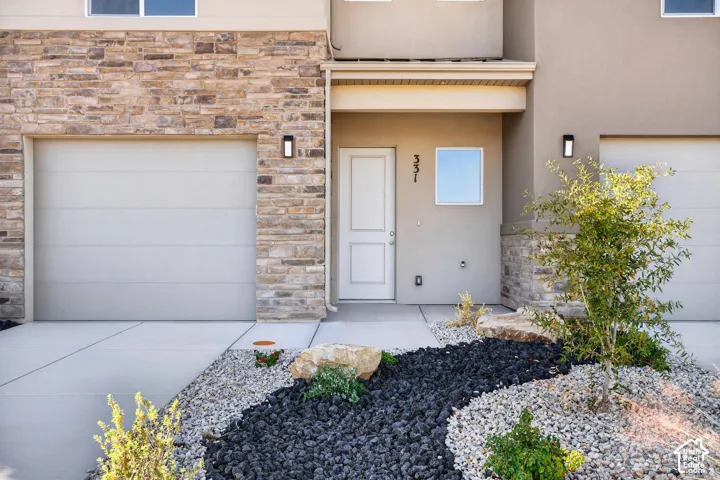 Multi-level exterior featuring stone veneer accents, neutral stucco siding, concrete driveway, recessed wall-mounted lighting, and xeriscaped front landscaping