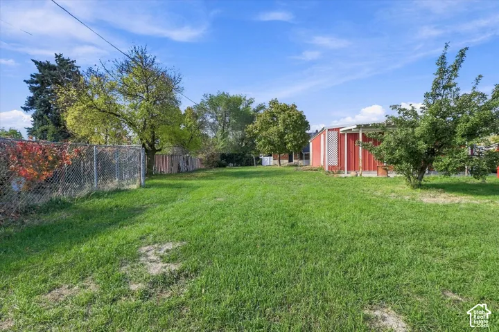 Expansive backyard featuring a large grass lawn, perimeter chain-link fencing, mature trees, and a detached red metal outbuilding