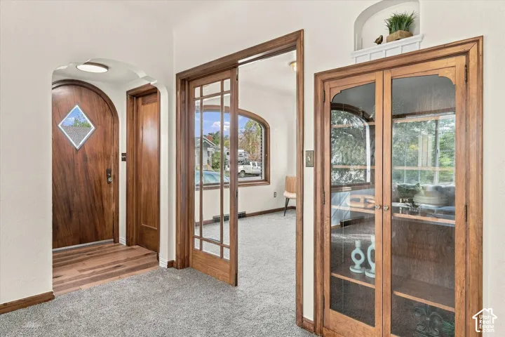 Arched entryway featuring a solid wood door with a diamond-shaped glass inlay, wood-trimmed glass French doors, and built-in wood cabinetry with glass-paned doors