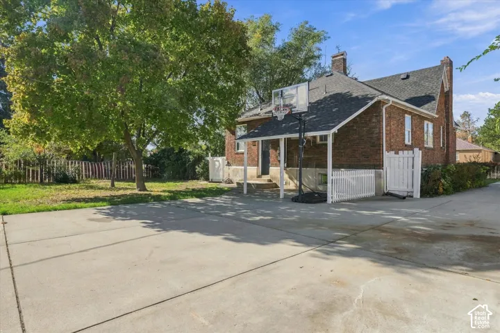Brick exterior featuring a concrete driveway, covered porch, and partial white fencing