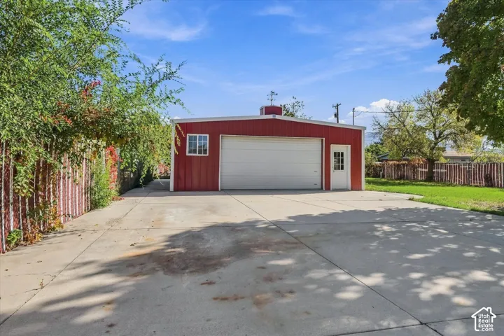 Detached garage featuring red metal siding, a wide concrete driveway, white sectional door, and a dedicated entry door