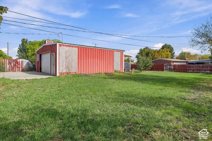 Detached garage with metal siding, roll-up door, lattice accents, and an expansive grass lawn with perimeter fencing
