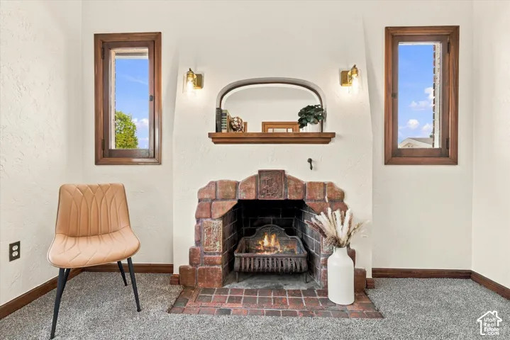Fireplace featuring ornate masonry surround, built-in wooden mantel, arched alcove, and dual wood-frame windows with brass-finish wall-mounted light fixtures
