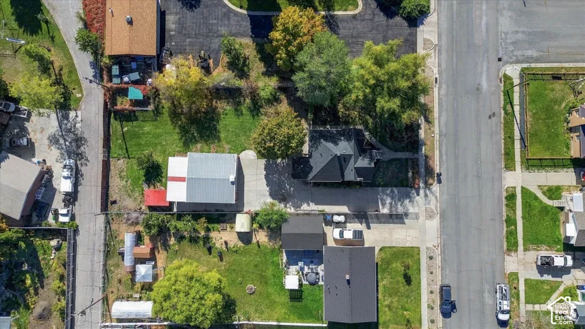 Aerial perspective of a property lot featuring mature trees, a detached garage, expansive lawn areas, and concrete driveway space