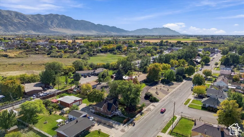 Aerial perspective featuring a multi-story residence with a pitched roof, prominent mountain backdrop, mature trees, and street-level access
