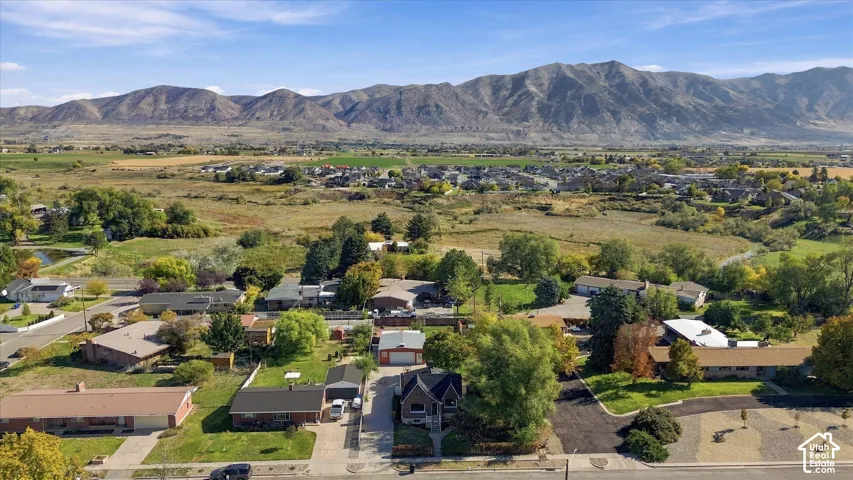 Aerial perspective showcasing a residential property with a detached garage, mature trees, an asphalt driveway, and a mountain range backdrop