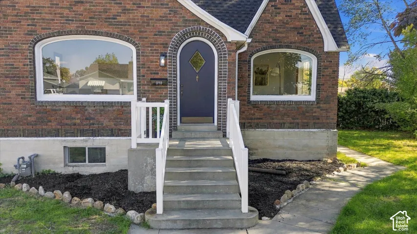 Brick exterior featuring an arched entryway, decorative diamond-pane front door, arched windows, and concrete front steps with white railings