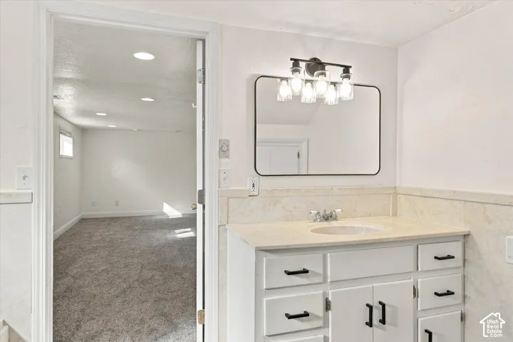 White vanity with matte black hardware, stone countertop, integrated sink, rectangular wall-mounted mirror, and multi-light vanity fixture