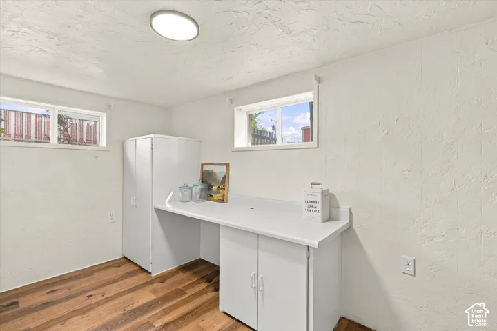 Textured walls featuring dual horizontal windows, wood-finish flooring, integrated white cabinetry with a solid surface countertop, and a flush-mount ceiling light