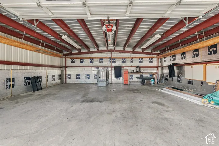 Spacious workshop featuring a concrete floor, exposed steel beam construction, high-clearance overhead garage door, and integrated fluorescent lighting