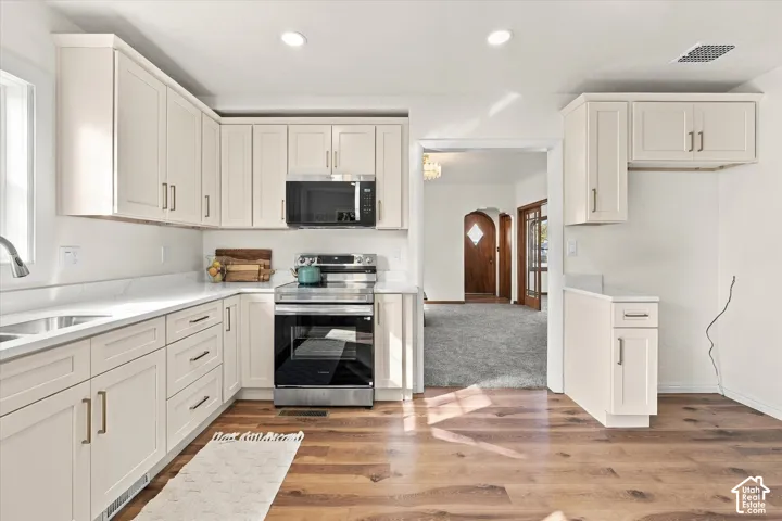Kitchen featuring shaker-style cabinetry, stainless steel appliances, light-toned stone countertops, and wood-finish flooring