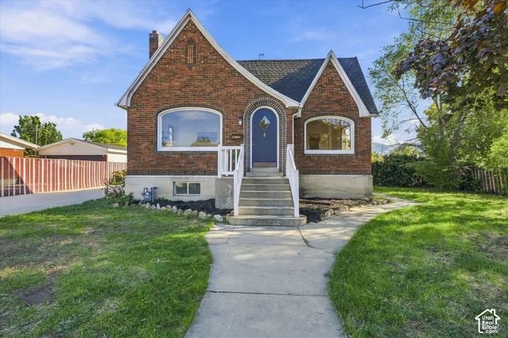 Classic brick exterior featuring an arched entryway, steep roof gables, large picture windows, and concrete front steps with white railings