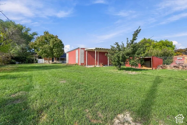 Expansive backyard featuring a large grass lawn, mature trees, chain-link fencing, and two metal outbuildings