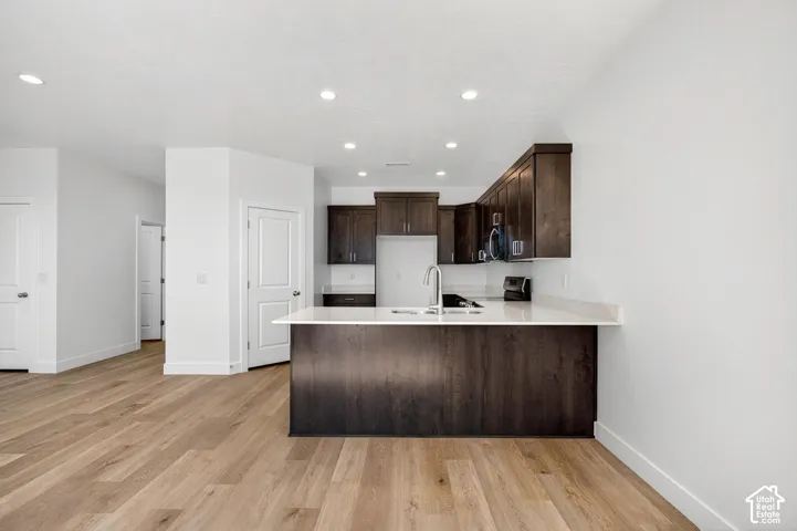 Kitchen featuring dark wood cabinetry, light-toned stone-finish countertops, wood-finish flooring, and recessed ceiling lighting