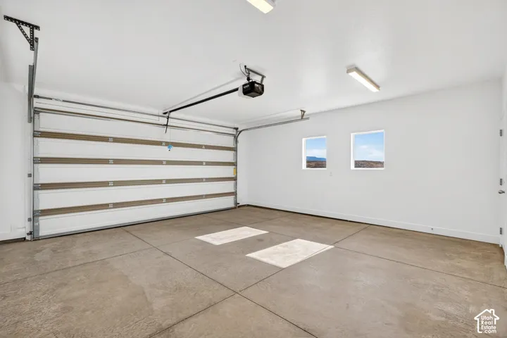 Finished garage space featuring a paneled roll-up door, neutral-toned concrete flooring, smooth-finish white walls, and dual square windows