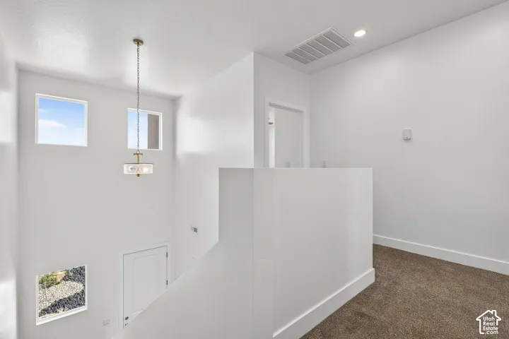 High-ceiling entryway featuring neutral wall-to-wall carpeting, three square windows, a multi-light pendant fixture, and a solid-core interior door