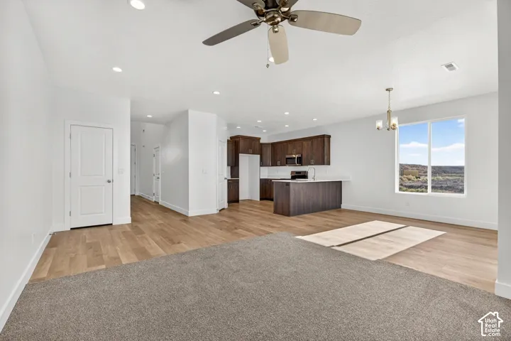 Open living area featuring wood-finish flooring, recessed lighting, ceiling fan, kitchen with dark-finish cabinetry, and a large window