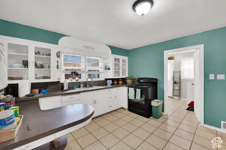Kitchen featuring white cabinetry with glass-front display uppers, built-in peninsula, tile flooring, and integrated window valance